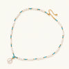 Beaded necklace with baroque pearls, turquoise stones, and gold accents featuring a large pearl pendant on white background.