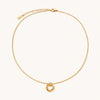 Delicate gold-plated necklace with three interlocking circle rings forming a minimalist knot pendant on cream background